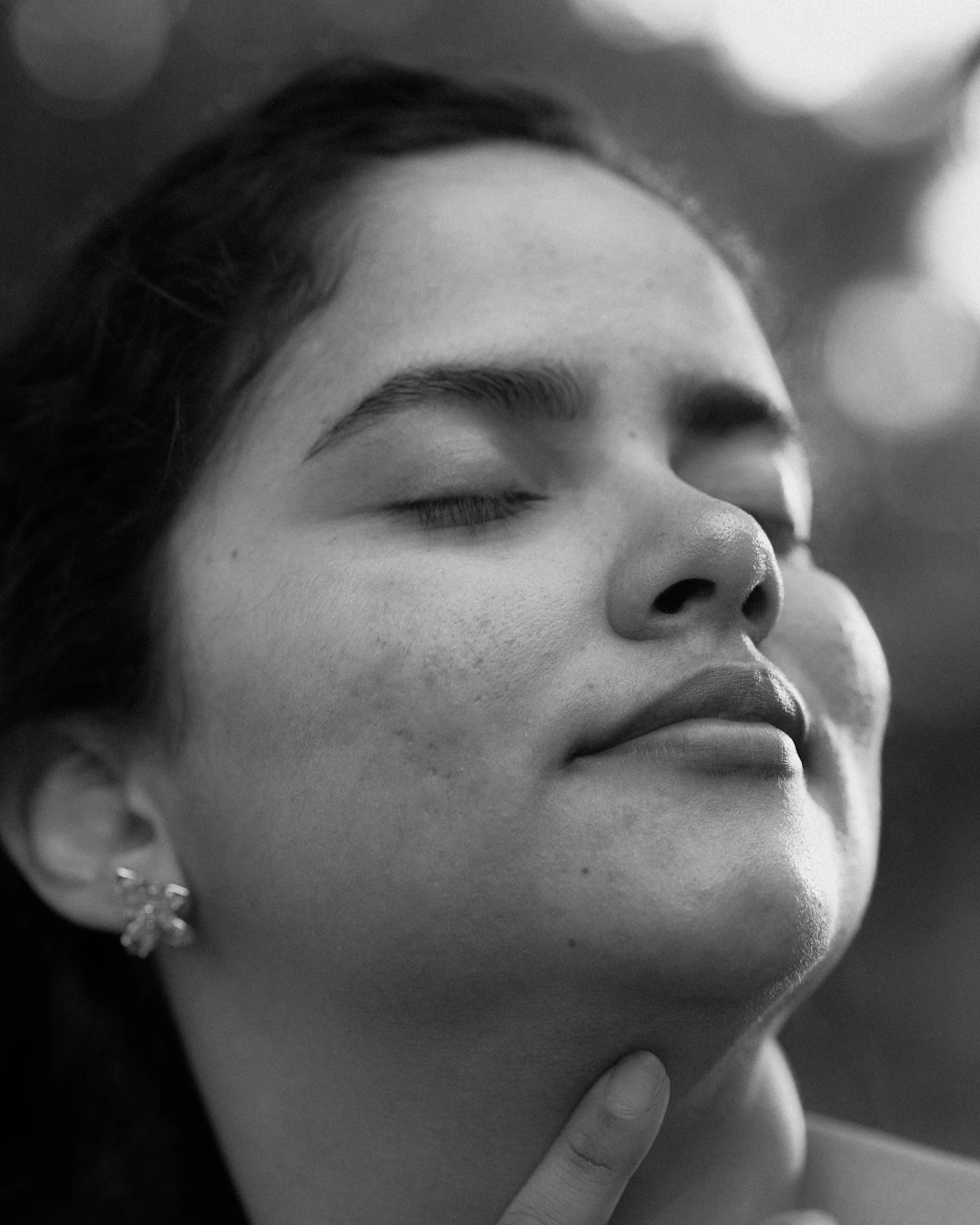 Mulher de olhos fechados, com o queixo levemente erguido e a mão no pescoço, em preto e branco.
