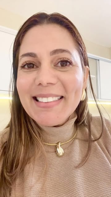 Simone Paixão sorrindo para a câmera, de gola alta bege e colar dourado.